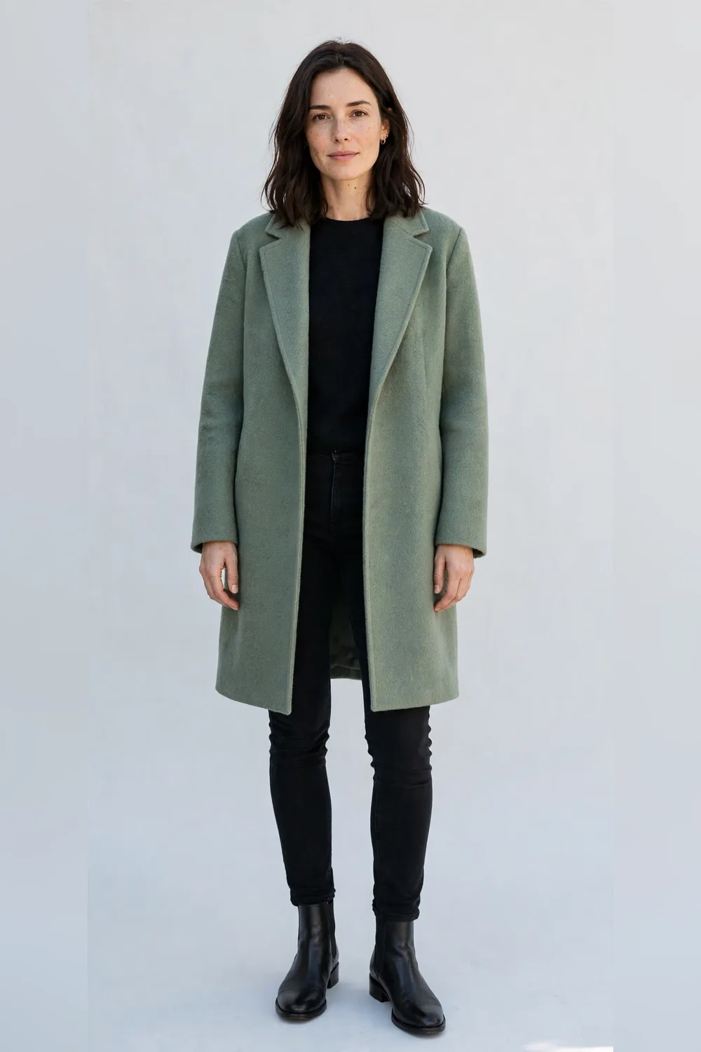 Sage green wool coat with black skinny jeans and black boots for women in their 30s