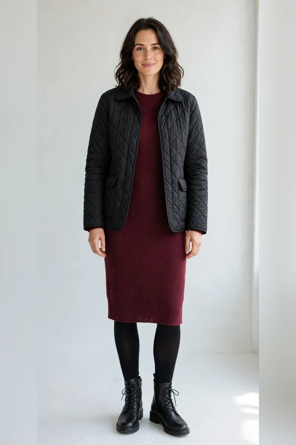 Black quilted jacket over a burgundy knit dress with black tights and boots for women in their 30s