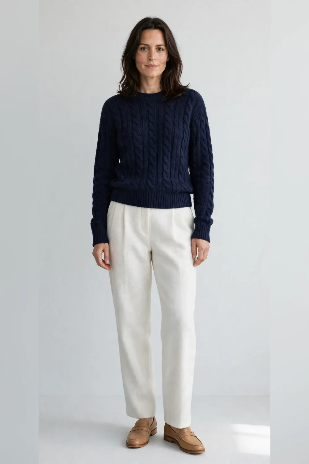 Navy cable-knit sweater with white wool trousers and tan loafers for women in their 30s