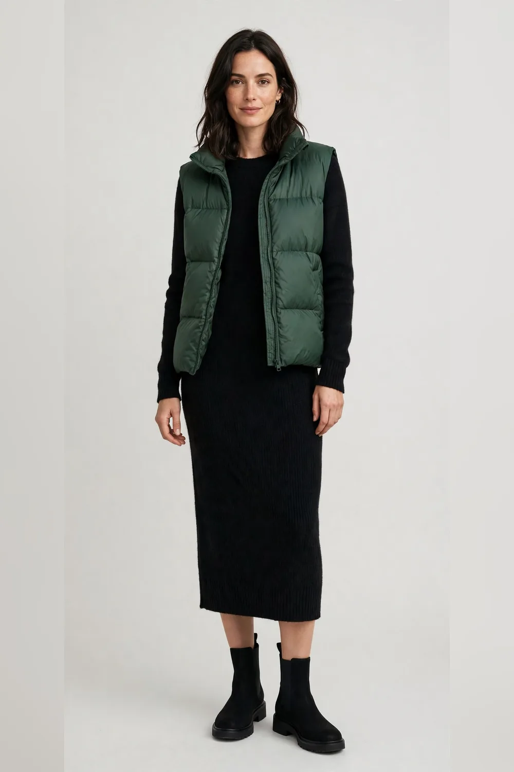 Forest green puffer vest over a black knit midi dress with black boots for women in their 30s