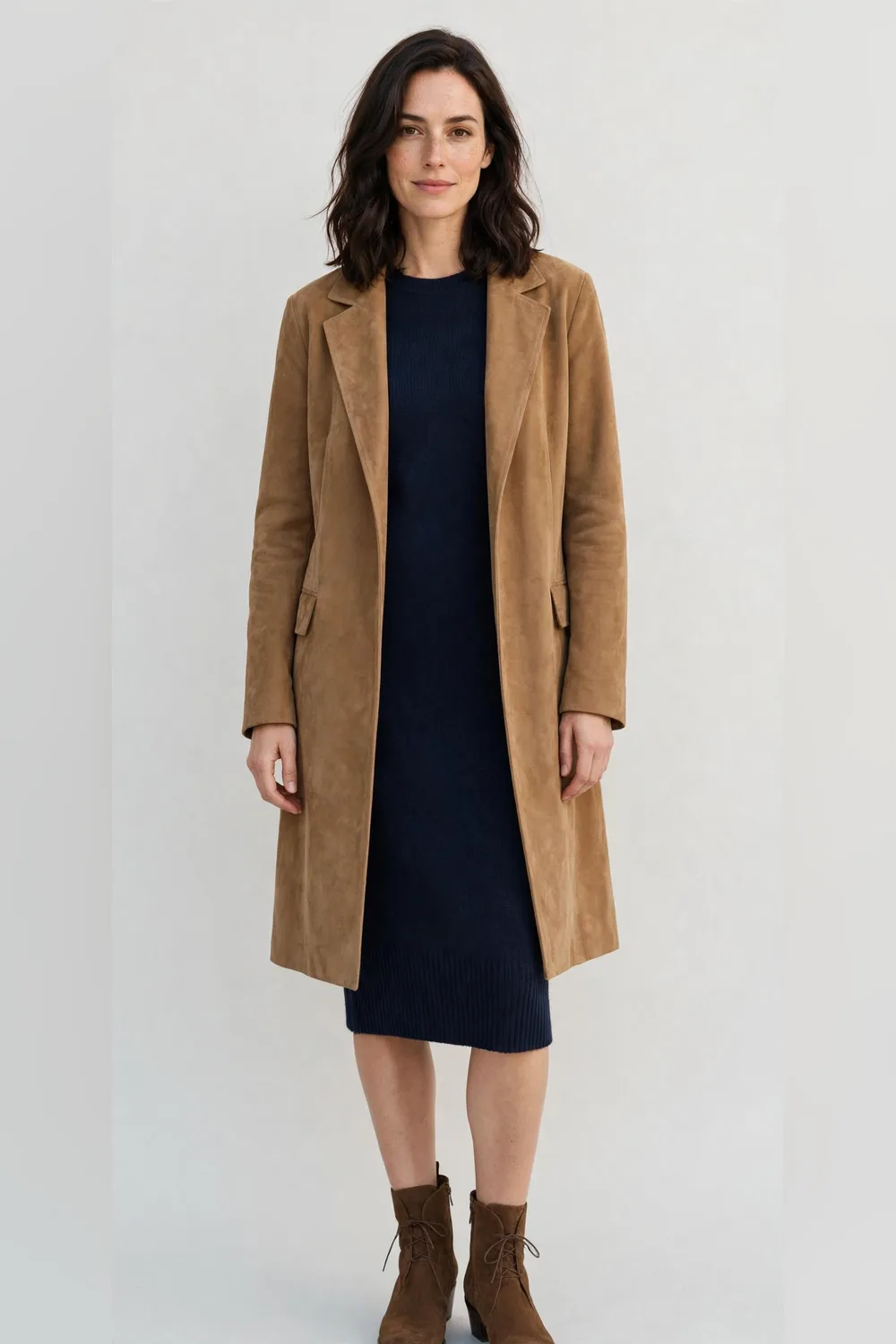 Tan suede coat over a navy knit dress with brown ankle boots for women in their 30s