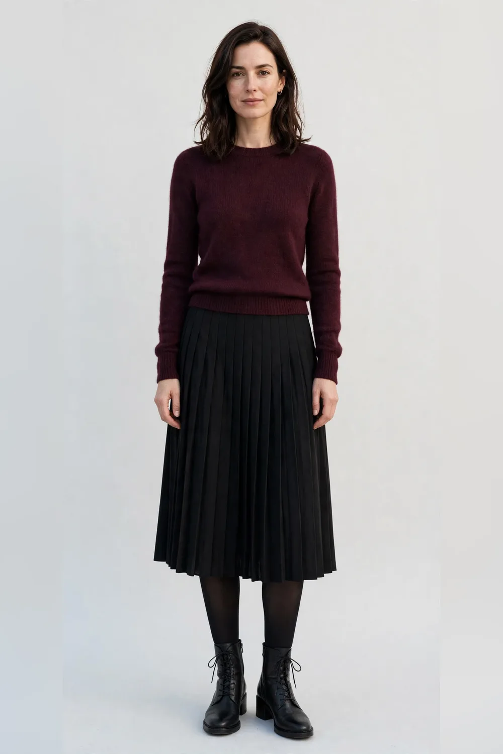 Wine knit sweater with a black pleated midi skirt and black tights and boots for women in their 30s
