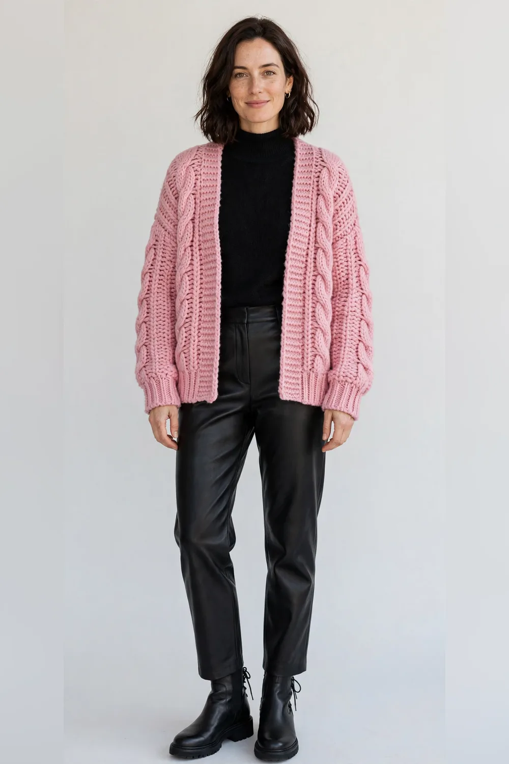 Pink chunky cardigan with black leather-look trousers and black ankle boots for women in their 30s